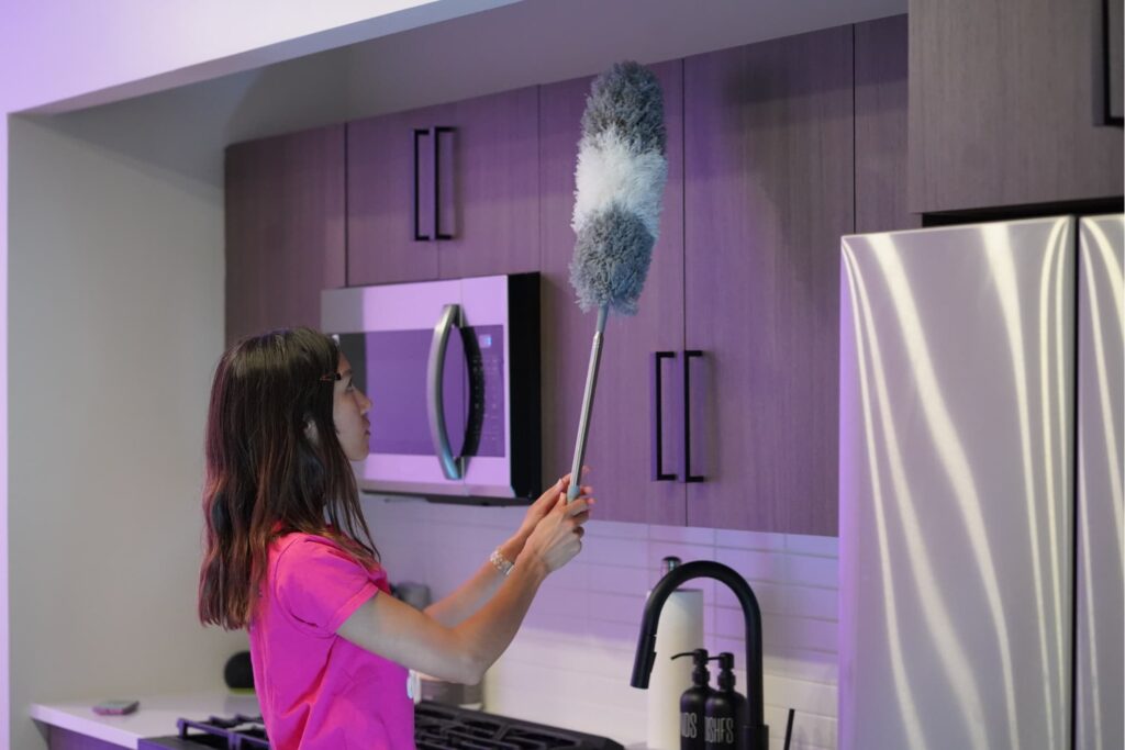 Cleaner dusting kitchen cabinets in a modern apartment.