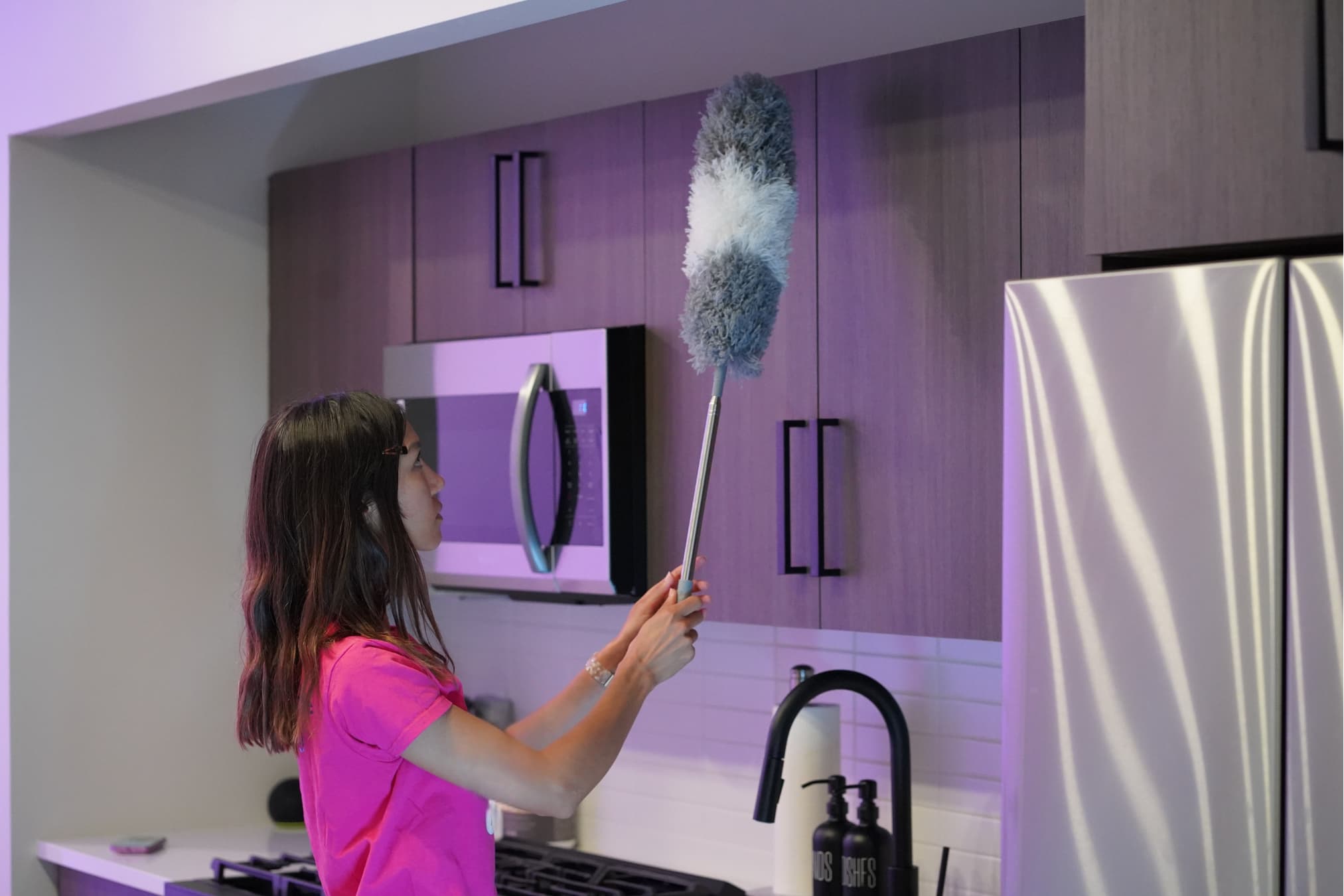 Cleaner dusting kitchen cabinets in a modern apartment.
